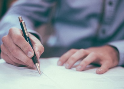 Hand signing a legal document with a pen on a desk